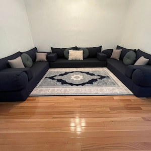 Puede incluir: Un sofá seccional azul oscuro con múltiples cojines y una alfombra estampada en el centro. El sofá está dispuesto en forma de U y tiene un diseño tradicional.