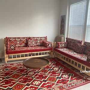 May include: Two wooden couches with red and white patterned cushions and a red and white patterned rug. The couches are in a room with white walls and a window with blinds.