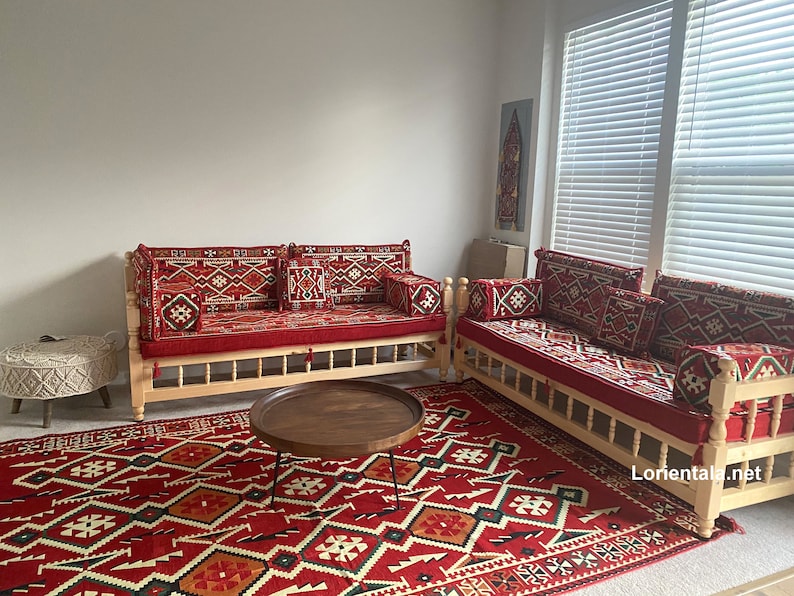 May include: Two wooden couches with red and white patterned cushions and a red and white patterned rug. The couches are in a room with white walls and a window with blinds.