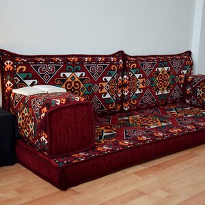May include: A red, patterned floor cushion with a geometric design. The cushion is made up of several smaller cushions, including two large back cushions and two smaller cushions. The cushion is perfect for sitting on the floor and is a great addition to any home.