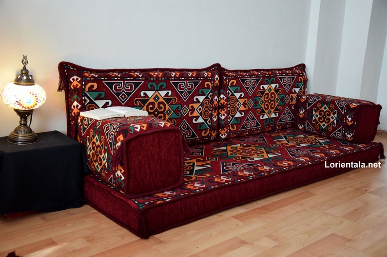May include: A red, patterned floor cushion with a geometric design. The cushion is made up of several smaller cushions, including two large back cushions and two smaller cushions. The cushion is perfect for sitting on the floor and is a great addition to any home.