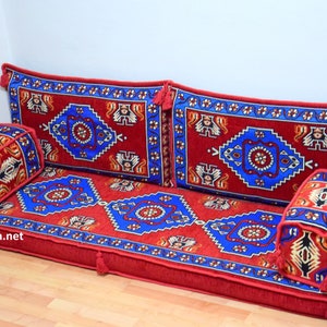 Puede incluir: Un coj&iacute;n de suelo rojo, azul y blanco con estampado con cuatro almohadas a juego. El coj&iacute;n est&aacute; hecho de una tela suave y mullida y tiene un dise&ntilde;o tradicional.