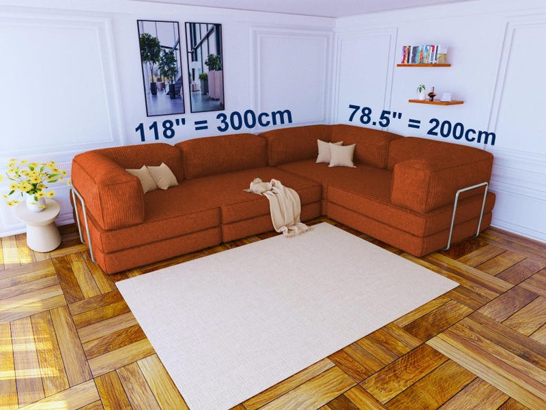 Pu&ograve; includere: Un grande divano angolare a forma di L in tessuto testurizzato color arancio bruciato con dettagli della struttura in metallo. Il divano misura 300 cm per 200 cm. Include diversi piccoli cuscini beige e una coperta beige drappeggiata.