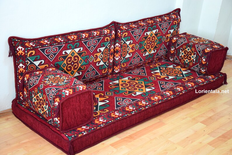 May include: A red floor cushion with a geometric pattern in shades of red, orange, green, and white. The cushion is made up of multiple pieces, including a large base cushion and several smaller cushions. The cushion is perfect for sitting on the floor or using as a sofa.