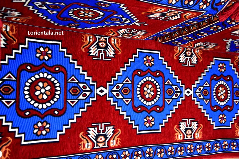 Puede incluir: Una alfombra roja, azul y blanca con un dise&ntilde;o geom&eacute;trico. La alfombra tiene un patr&oacute;n repetitivo de cuadrados y c&iacute;rculos.