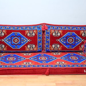 Puede incluir: Un coj&iacute;n de suelo rojo y azul con estampado con cuatro almohadas a juego. El coj&iacute;n est&aacute; hecho de una tela suave y mullida y tiene un dise&ntilde;o tradicional. Las almohadas son cuadradas y tienen borlas en las esquinas.