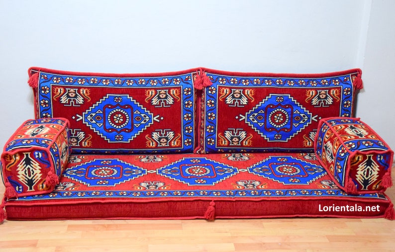 Puede incluir: Un coj&iacute;n de suelo rojo y azul con estampado con cuatro almohadas a juego. El coj&iacute;n est&aacute; hecho de una tela suave y mullida y tiene un dise&ntilde;o tradicional. Las almohadas son cuadradas y tienen borlas en las esquinas.
