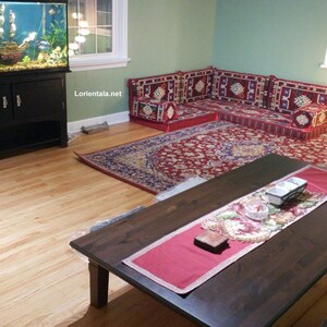 May include: A living room with a large fish tank, a dark wood coffee table, and a red and blue patterned rug. The room is decorated with a traditional Middle Eastern style seating arrangement, featuring colorful cushions and pillows.