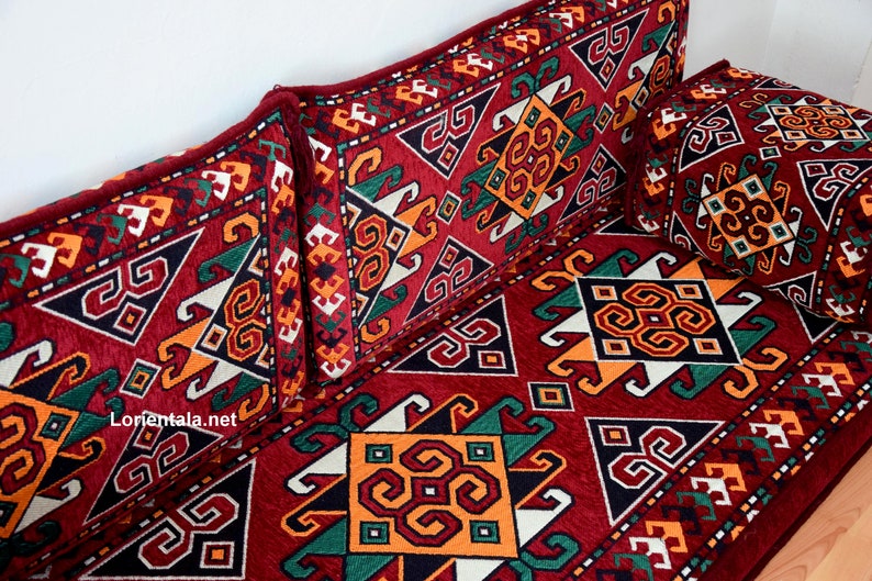 May include: A red, green, white, and orange patterned floor cushion with two matching pillows. The cushion and pillows feature a geometric design.