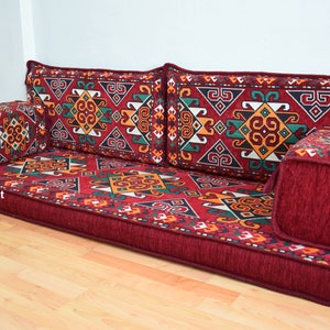 May include: A red, patterned floor cushion with a geometric design. The cushion is made up of several pieces, including two large back cushions, a smaller front cushion, and two armrests. The cushion is perfect for sitting on the floor and is a great addition to any home.