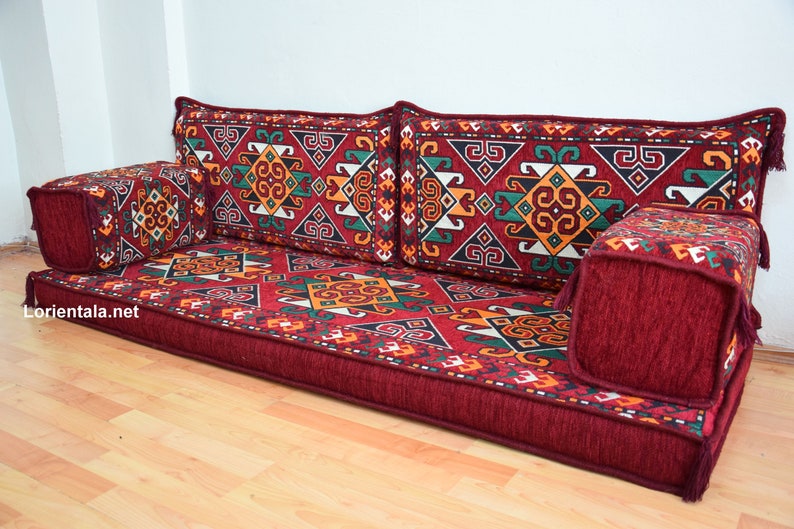 May include: A red, patterned floor cushion with a geometric design. The cushion is made up of several pieces, including two large back cushions, a smaller front cushion, and two armrests. The cushion is perfect for sitting on the floor and is a great addition to any home.
