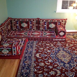 May include: A red and blue patterned corner sofa with a matching ottoman and a red rug with a floral design. The sofa is made up of individual cushions and is perfect for lounging.