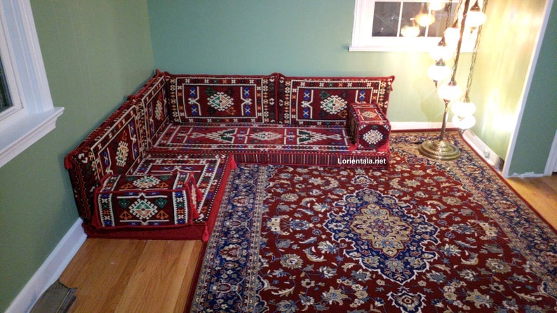 May include: A red and blue patterned corner sofa with a matching ottoman and a red rug with a floral design. The sofa is made up of individual cushions and is perfect for lounging.