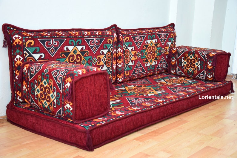 May include: A red floor cushion with a geometric patterned fabric. The cushion is made up of multiple pieces, including a large rectangular base and several smaller square cushions. The fabric features a mix of red, green, yellow, and white colors.