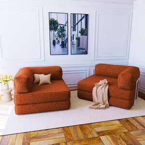 Pu&ograve; includere: Due poltrone modulari senza braccioli rivestite in un tessuto testurizzato color arancio bruciato. Ogni poltrona presenta un design basso con un solo bracciolo laterale, seduta quadrata e schienale. Una include due piccoli cuscini beige, l'altra un plaid beige.