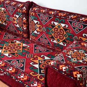 May include: A red, patterned floor cushion with geometric designs in shades of green, orange, and white. The cushion is made of a soft, plush fabric and has a traditional Moroccan style.