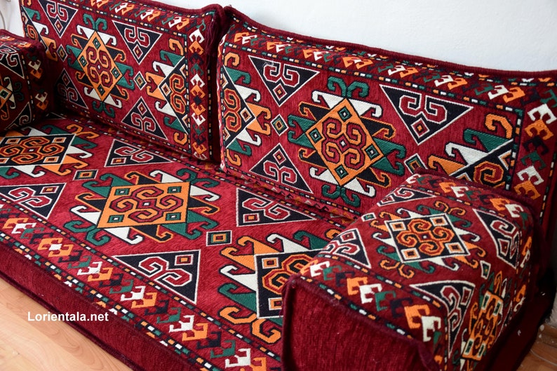 May include: A red, patterned floor cushion with geometric designs in shades of green, orange, and white. The cushion is made of a soft, plush fabric and has a traditional Moroccan style.
