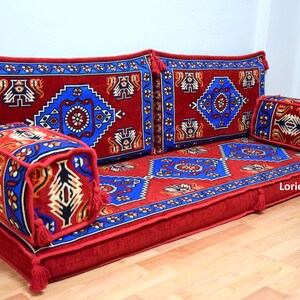Puede incluir: Un conjunto de cojines de suelo con estampado rojo y azul con borlas. Los cojines est&aacute;n dispuestos en forma de sof&aacute; con dos cojines de respaldo y un coj&iacute;n de asiento largo. Hay un coj&iacute;n cuadrado m&aacute;s peque&ntilde;o en la parte delantera. Los cojines tienen un dise&ntilde;o turco tradicional.