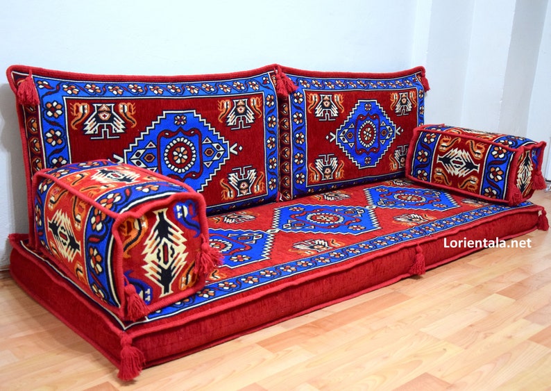 Puede incluir: Un conjunto de cojines de suelo con estampado rojo y azul con borlas. Los cojines est&aacute;n dispuestos en forma de sof&aacute; con dos cojines de respaldo y un coj&iacute;n de asiento largo. Hay un coj&iacute;n cuadrado m&aacute;s peque&ntilde;o en la parte delantera. Los cojines tienen un dise&ntilde;o turco tradicional.