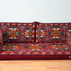 May include: A red, patterned floor cushion with a geometric design. The cushion is made up of several pieces, including a large rectangular base, two long rectangular back cushions, and two smaller square cushions. The cushion is perfect for sitting on the floor or using as a sofa.
