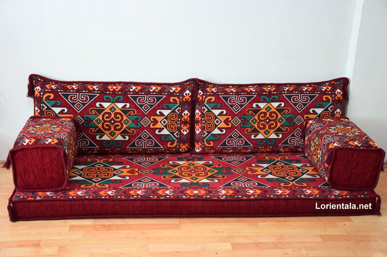 May include: A red, patterned floor cushion with a geometric design. The cushion is made up of several pieces, including a large rectangular base, two long rectangular back cushions, and two smaller square cushions. The cushion is perfect for sitting on the floor or using as a sofa.
