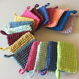 Peut inclure: Une collection de dessous de plat carrés et colorés, tricotés dans diverses nuances, dont le rose, le bleu, le vert et le jaune. Chaque dessous de plat est doté d'une boucle pour être suspendu. Les dessous de plat sont disposés en cercle.