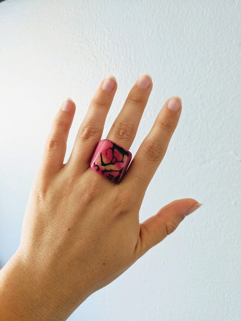 May include: A square pink ring with a marbled design in shades of pink, orange, and black.