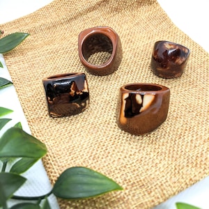May include: Four ceramic rings with brown and white glaze. The rings are displayed on a brown burlap surface.