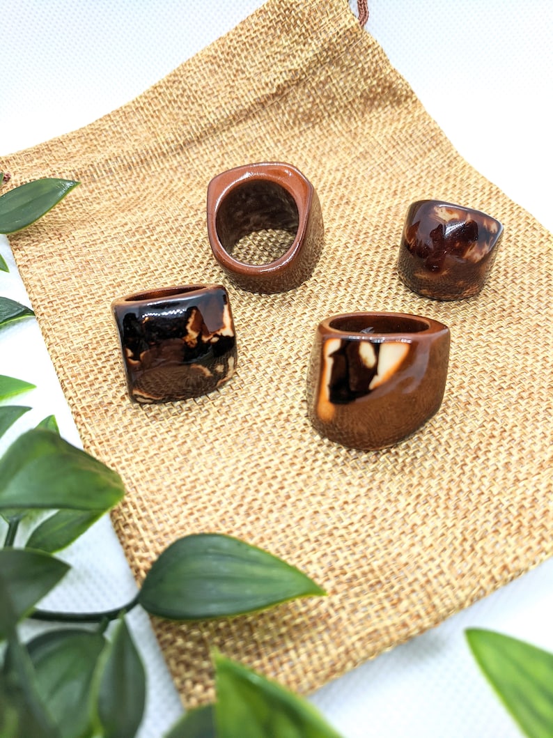 May include: Four ceramic rings with brown and white glaze. The rings are displayed on a brown burlap surface.
