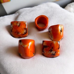 May include: Five orange and white resin rings with a marbled pattern. The rings are all different shapes and sizes.