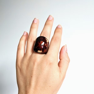 May include: A large, brown and cream colored ring with a unique marbled pattern. The ring is made of resin and is worn on a finger.