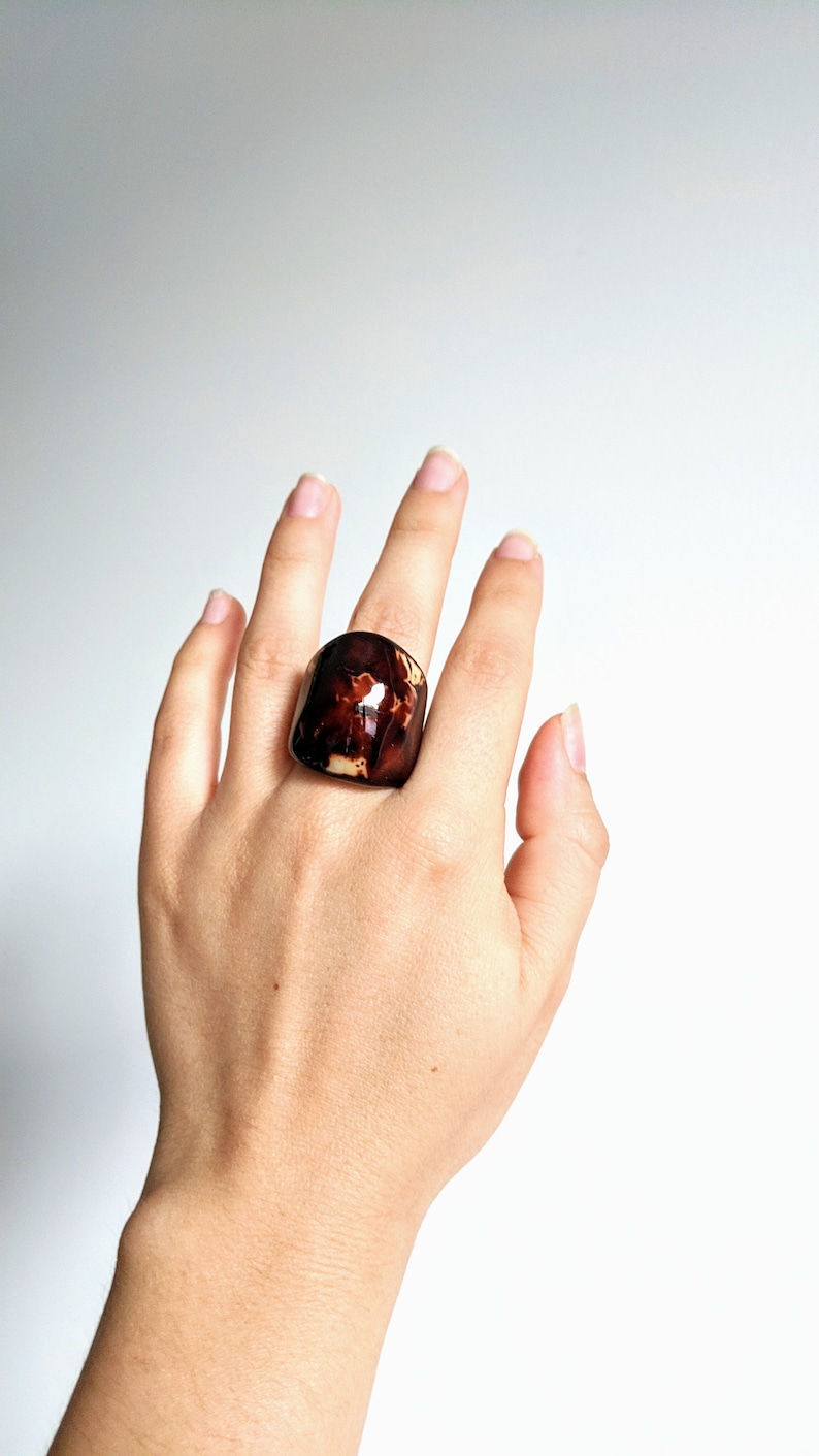 May include: A large, brown and cream colored ring with a unique marbled pattern. The ring is made of resin and is worn on a finger.