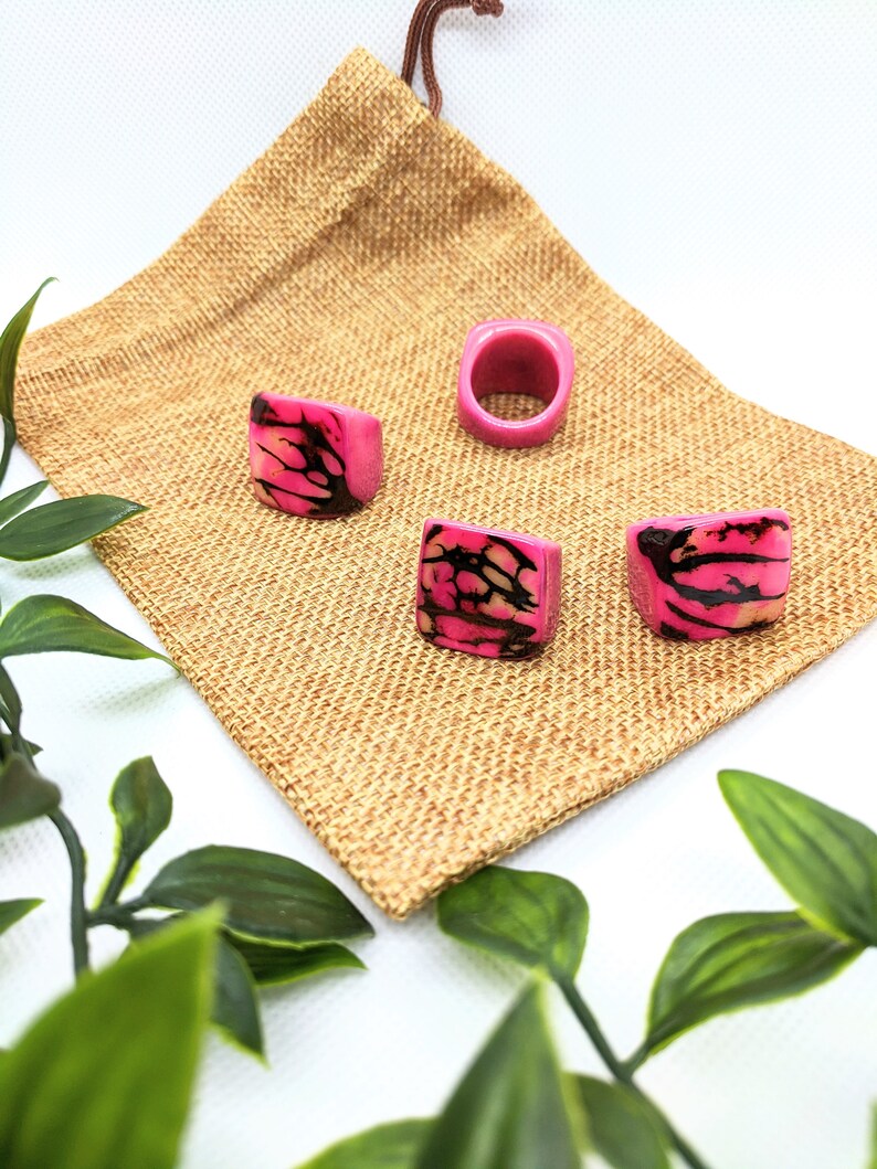 May include: Four pink and black patterned rings on a brown burlap bag. The rings are made of wood and have a unique design.