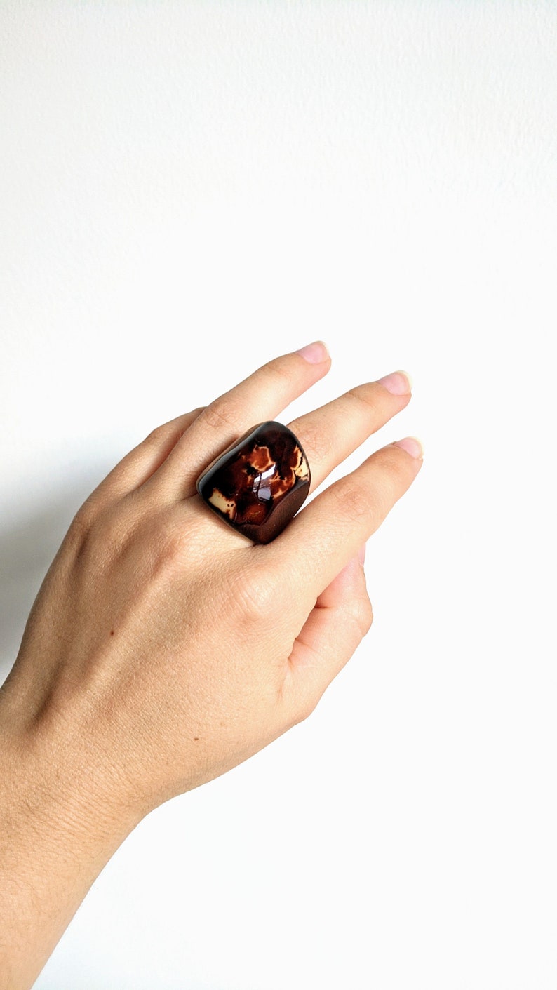 May include: A large, brown and cream resin ring with a unique marbled pattern. The ring is worn on a person's finger.