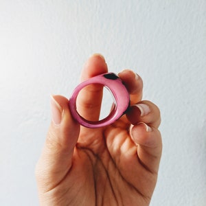 May include: A pink and black resin ring with a smooth, rounded surface.