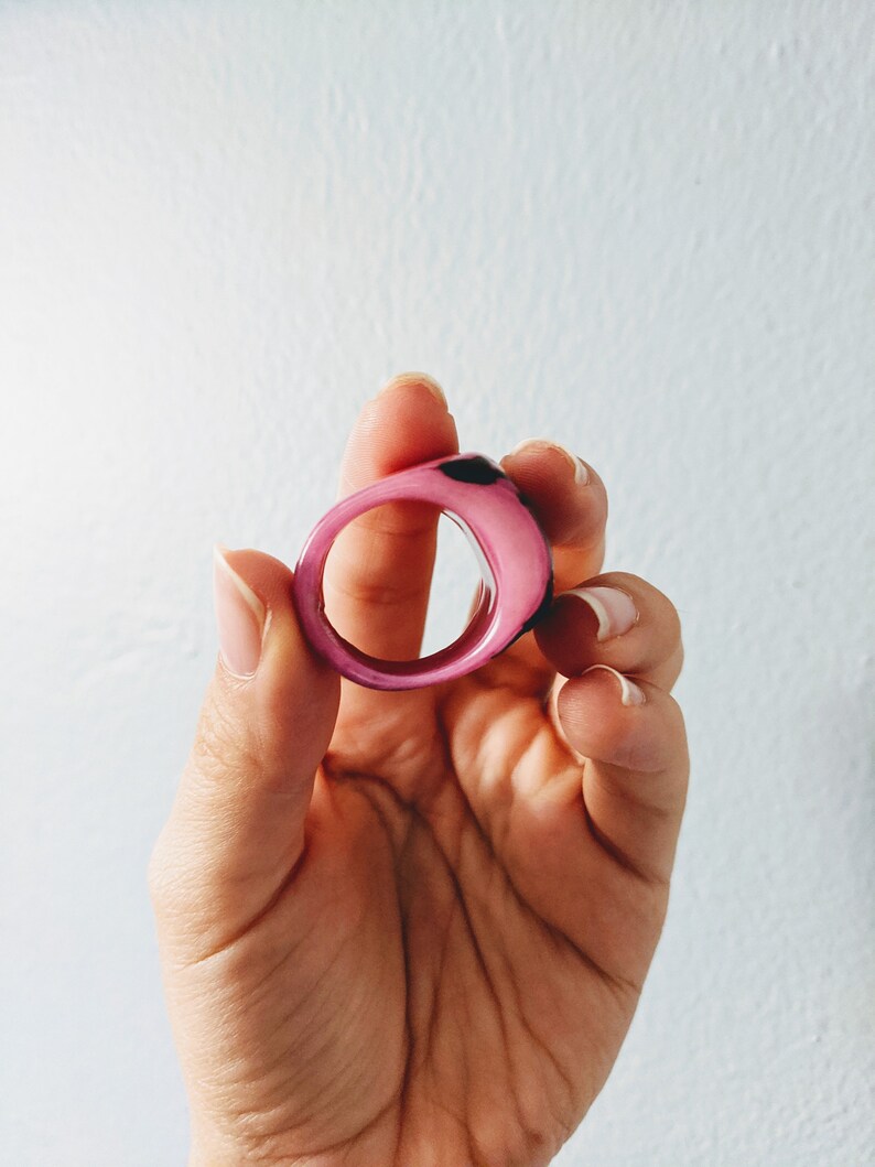 May include: A pink and black resin ring with a smooth, rounded surface.