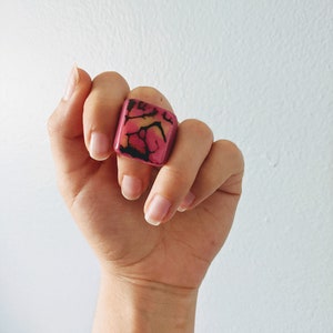 May include: A square-shaped ring with a pink and black marbled design.