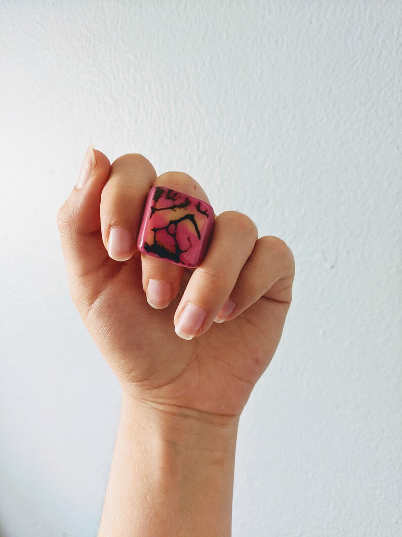 May include: A square-shaped ring with a pink and black marbled design.