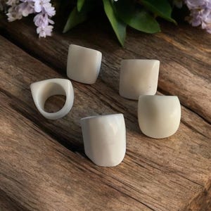 May include: Five white rings made of bone or ceramic on a wooden surface. The rings are all different shapes and sizes.