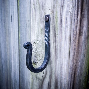 May include: A black metal hook with a twisted design is attached to a weathered wooden post.