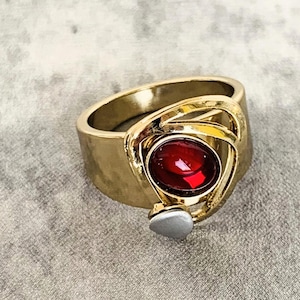 May include: Gold ring featuring a red gemstone set within a swirling design.