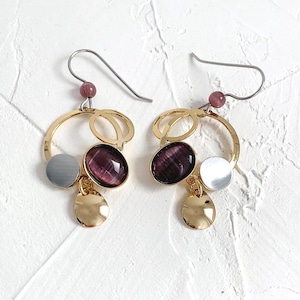 May include: Gold hoop earrings with a purple stone, a silver circle, and a gold charm. The earrings have a silver hook.