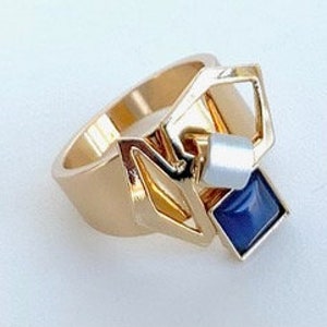 May include: Gold ring with a geometric design featuring a blue stone and a white cube.