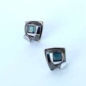 May include: A pair of silver-tone square stud earrings with a teal-colored square center and a small, round accent. The earrings are set against a white background.