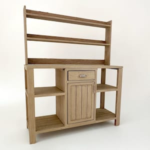 May include: A light brown wooden miniature hutch featuring two open upper shelves with textured edges, a central cabinet with a single vertical-slatted door, one small drawer with a silver handle, and two open side shelving units on each side.