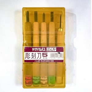 May include: A set of five wood carving tools in a clear plastic case. The tools have wooden handles and metal blades. The case has Japanese text on a purple and white label.