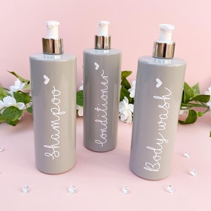 May include: Three grey plastic pump bottles with white labels. The labels read "shampoo", "conditioner", and "body wash".