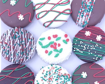 May include: Nine chocolate-covered cookies decorated with red, green, and white sprinkles, lines, and designs. The cookies are arranged in a circle on a white surface.