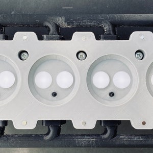 May include: A white plastic 3D printed model of a four-cylinder engine with black plastic tubing and a white air filter.