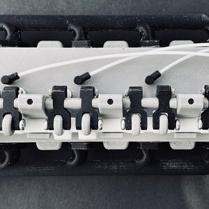 May include: A close-up of a 3D printed model of a small engine with white wires and black and grey components.